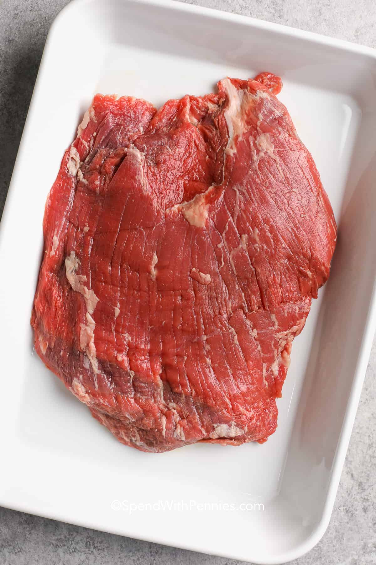 uncooked flank steak in a white baking dish