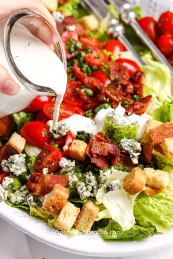 pouring a creamy herbed dressing over a blt salad