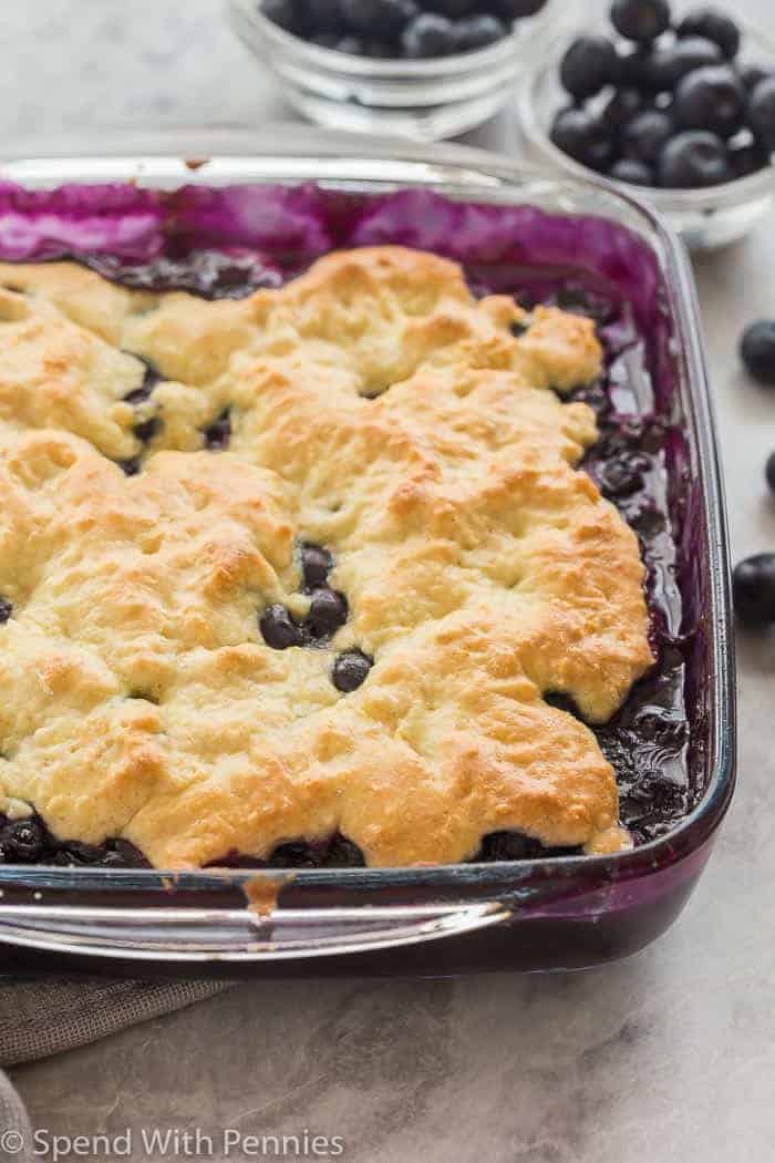 blueberry cobbler in glass pan with bowls of blueberries in the background