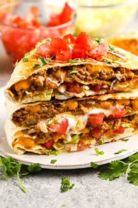 Crunchwrap Supreme stacked on a plate with diced tomatoes and cilantro