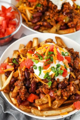 plate full of Chili Cheese Fries with a bowl of tomatoes in the back