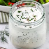 Homemade ranch dressing in a jar with a spoon and a salad in the background