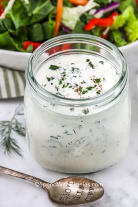 Homemade ranch dressing in a jar with a spoon and a salad in the background