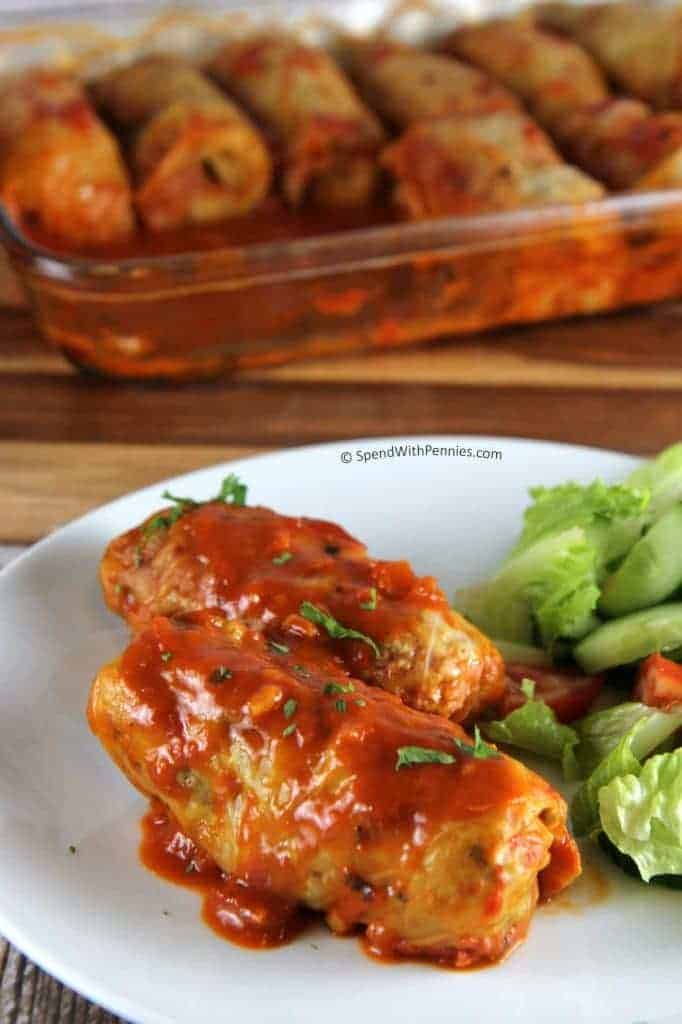 Two cabbage rolls and a salad on a white plate, with baking dish of cabbage rolls in the background