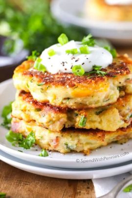 Loaded Mashed Potato Cakes with sour cream and green onions and parsley in the background on a wood table