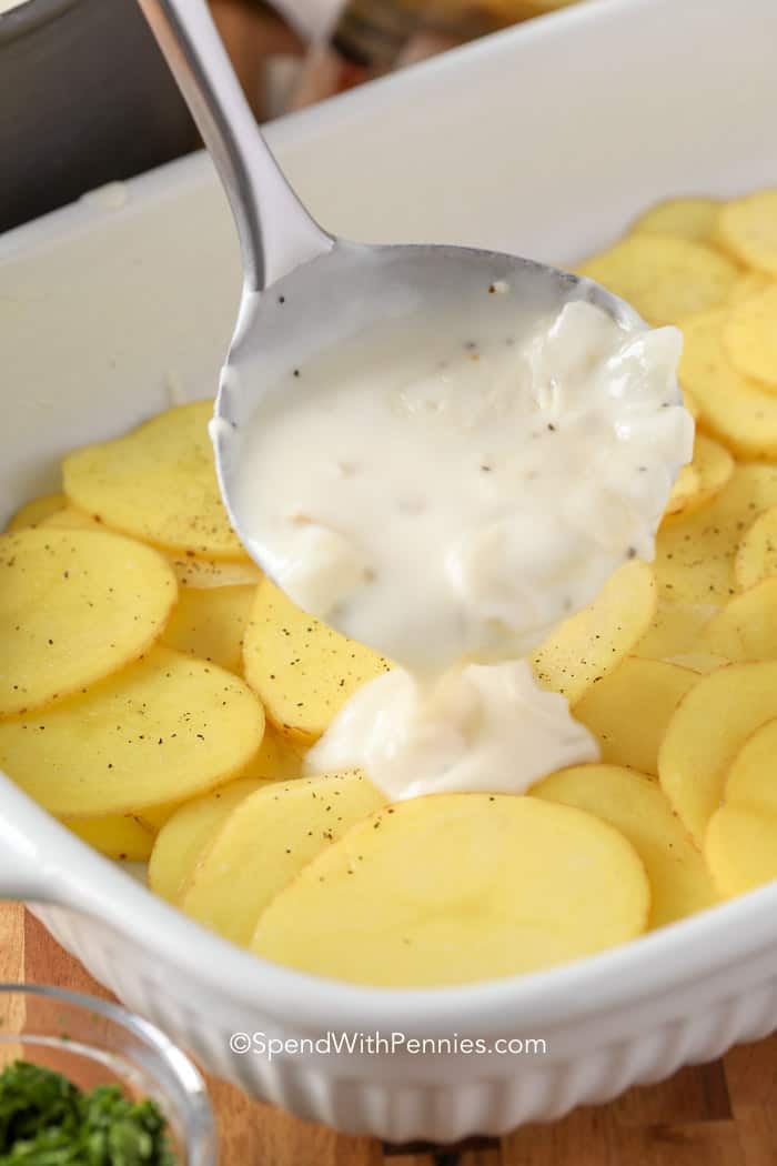 Sauce being poured over sliced potatoes in a casserole dish