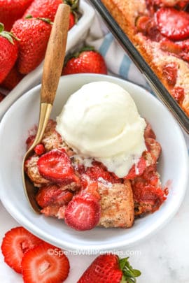 Strawberry Rhubarb Cobbler in a white bowl with vanilla ice cream and a spoon