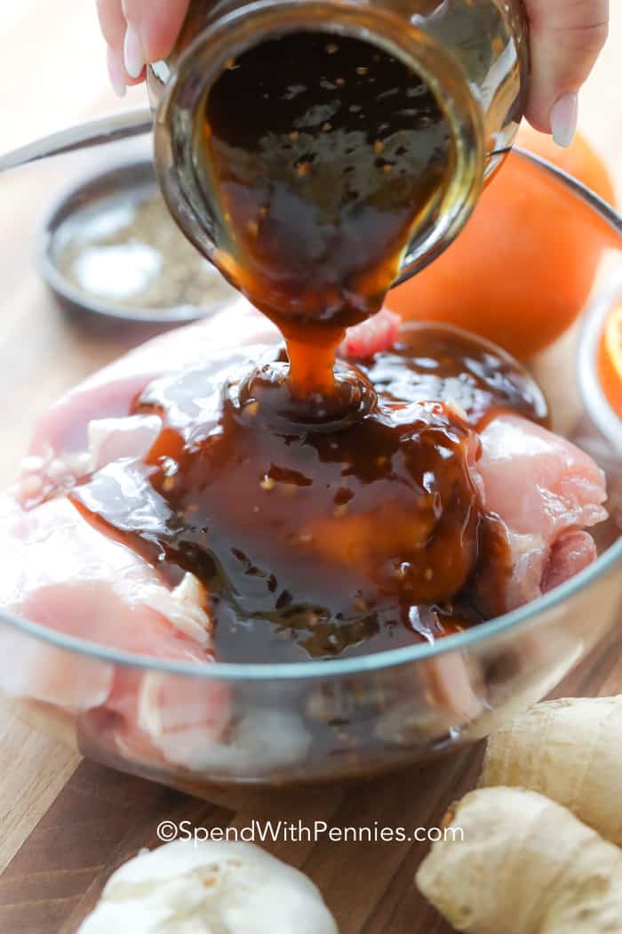 Pouring homemade teriyaki sauce over raw chicken in a clear glass bowl